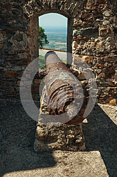 Old rusty iron cannon aiming through window in stone wall