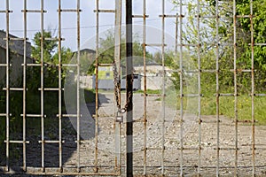 Old rusty iron gate on chain and lock. Closed metal gates. Protection, security and safety concept. padlock on metal gate