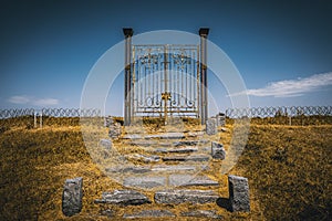 Old rusty iron gate in the middle of a field leading to nowhere. Concept of purgatory, limits, frontiers and freedom