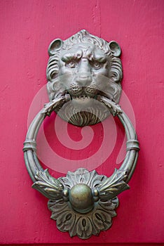 Old golden iron lion head door knocker on a wooden pink door. Mdina, Malta