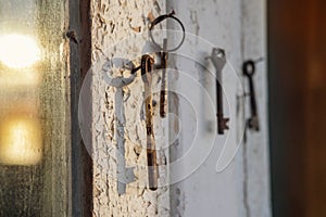 Old rusty key on the wooden door frame with broken white paint with a blurred reflection of a sunset on a dirty glass