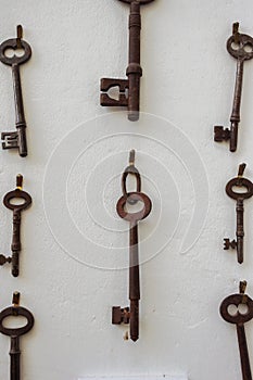 Old rusty keys hanging on a white wall.