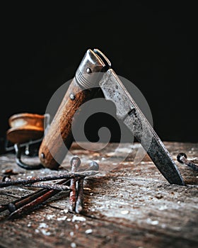 Isolated old pocket knife sticking in a wooden plate with rusty nails in foreground