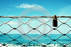 Old rusty lock over iron fence with blue sea background.