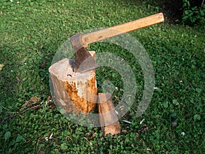 Old rusty metal axe with wooden handle on a fire wood cutting block on green grass. Old style equipment
