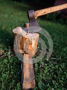 Old rusty metal axe with wooden handle on a fire wood cutting block on green grass. Old style equipment