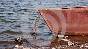 Old rusty metal boat chained on a river bank on sunny day