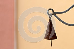 An old rusty metal cone shaped bell is hanging suspended in air outside against a blank tan wall background photo