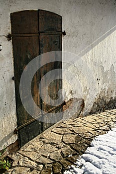 Old rusty metal door with two latches, stone pathway and snow