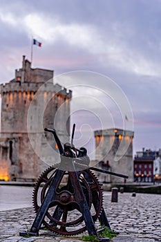 old rusty metal gear wheel in the port of la rochelle. it stands in front of the medieval city's famous towers