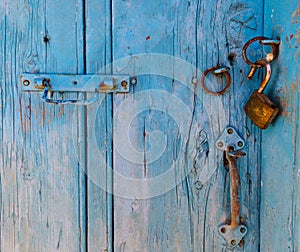 Old rusty metal latch with a padlock hanging on a blue door