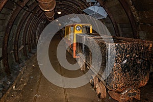 Old and rusty metal mine train with wagons in mine tunnel with wooden timbering