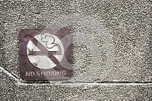 Old rusty metal no smoking allowed sign on dirty pebbles stone wall texture in public place