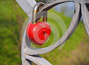 Old rusty metal red heart lock, the romantic symbol of never ending love hanging on the fence of bridge