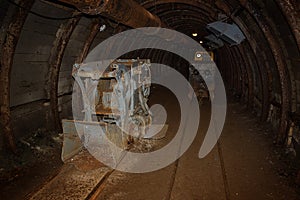 Old and rusty mine machine and train with wagons in mine shaft with wooden timbering