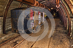 Starý a rezavý důlní vlak pro přesun personálu zaparkovaný v důlním tunelu s dřevěným roubením
