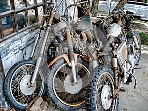 Old, rusty motorcycles stored outside a worn-down garage with peeling paint