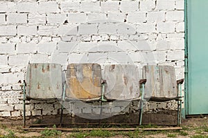 Old rusty movie theater chairs stand against a brick wall