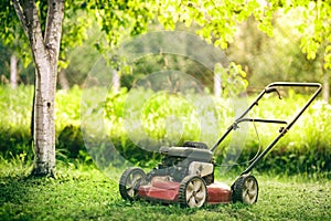 Old rusty mower on the newly mown grass in backyard. Agricultural machinery