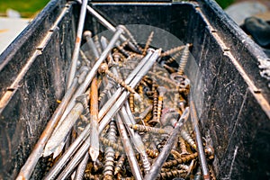 Old rusty nails and self-tapping screws in a plastic container, close-up. Used fasteners after dismantling