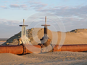 An old rusty oil pipeline in the desert with valves. Pipeline for oil or gas at dawn. Mining of natural resources