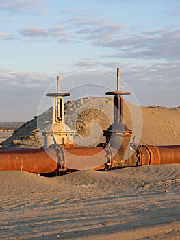 An old rusty oil pipeline in the desert with valves. Pipeline for oil or gas at dawn. Mining of natural resources