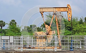 Old rusty oil pump jack extracting crude oil and natural gas from well in green background