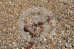 Old rusty orange brown nautical chain with ring lying on shingle beach