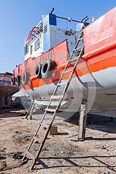 Old rusty orange ship under repairing on grungy dry dock in shipyard in old shipbuilding plant