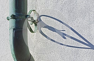 Old rusty oxidized copper downpipe against a plaster wall with shadow