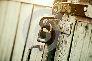 An old rusty padlock closes the wooden old gate on a sunny day. Safety