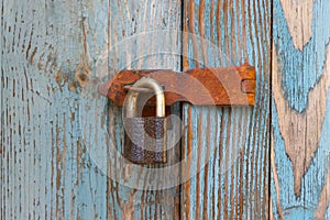 An old rusty padlock on an old cracked wooden door covered with old peeled blue paint