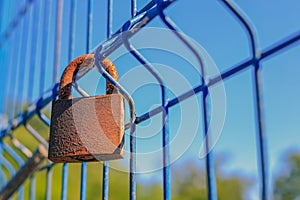 An old rusty padlock hanging on a blue grille