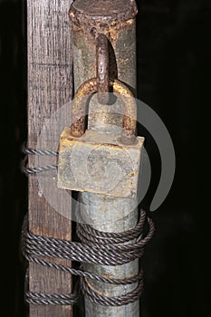 Rusted padlock on old metal pole with twisted rope