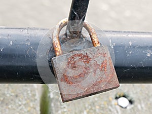Old rusty padlock up close locked on black metal gate