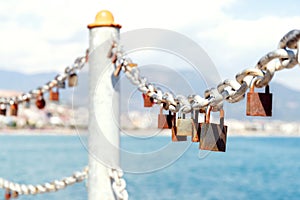 Old rusty padlocks on chain on metal railing against the city and blue sea on sunny day. Close-up. Selective focus. Blurred