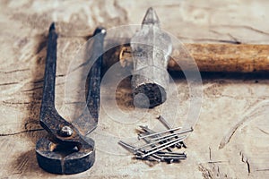 Old rusty pincers, nails and hammer on a wooden background