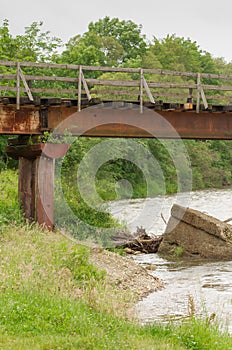 An old, rusty railway bridge over the river with old wooden beams.