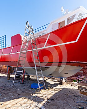 Old rusty red ship under repairing on grungy dry dock in shipyard in old shipbuilding plant