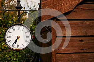 Old rusty retro style clock on a metal frame housing hanging on a side of a wooden barn,