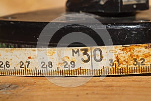 Old rusty ruler with black numbers on a working wooden table. vintage measuring tape close up. industrial background