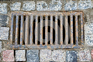 An old rusty sewer grate in a stone pavement on a city street