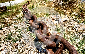 Old rusty ship anchor metal chain laying on the ground.