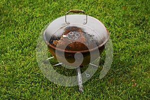 Old rusty small barbeque cooker in a garden. Cheap metal cooking device. Worn out budget way to cook food