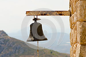 Old rusty steel big bell from church with rope on stone wall in