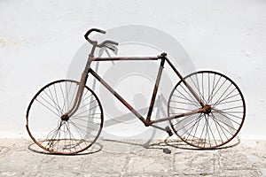 Old, rusty, superannuated bicycle wreck stands next to a pure white wall outdoor.