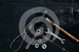 Old, rusty tools lying on a black wooden table. Hammer, chisel, metal scissors, wrench.