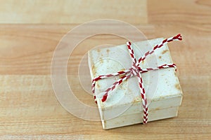 Old rusty vintage present gift box with stains tied with red white striped rope on wooden background