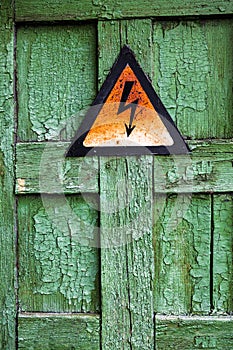 Old rusty warning high voltage sign on cracked wooden surface