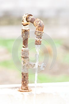 Old rusty water tap with flowing water in the garden